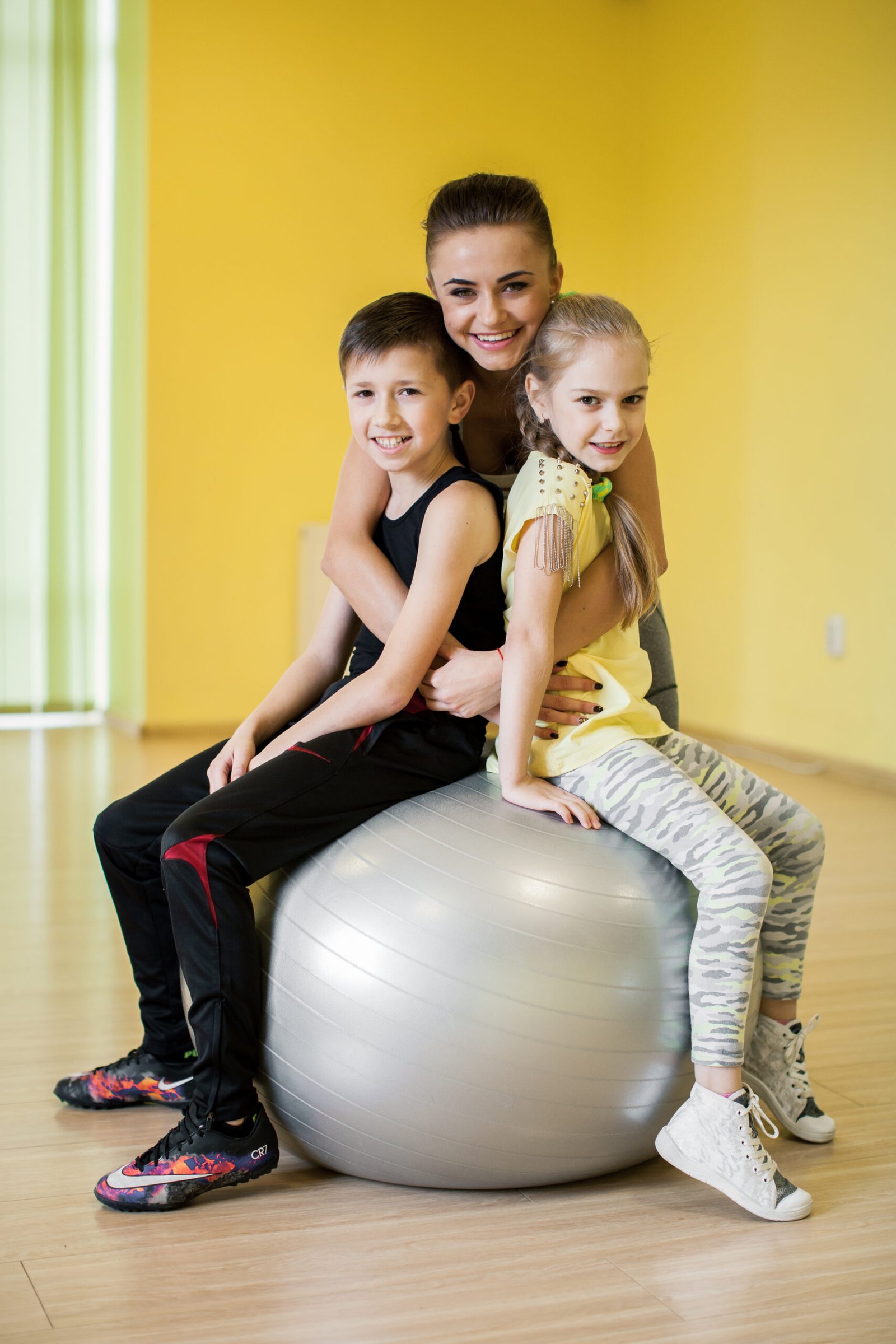 Home 10 Mother exercising with two children on a fitness ball at home
