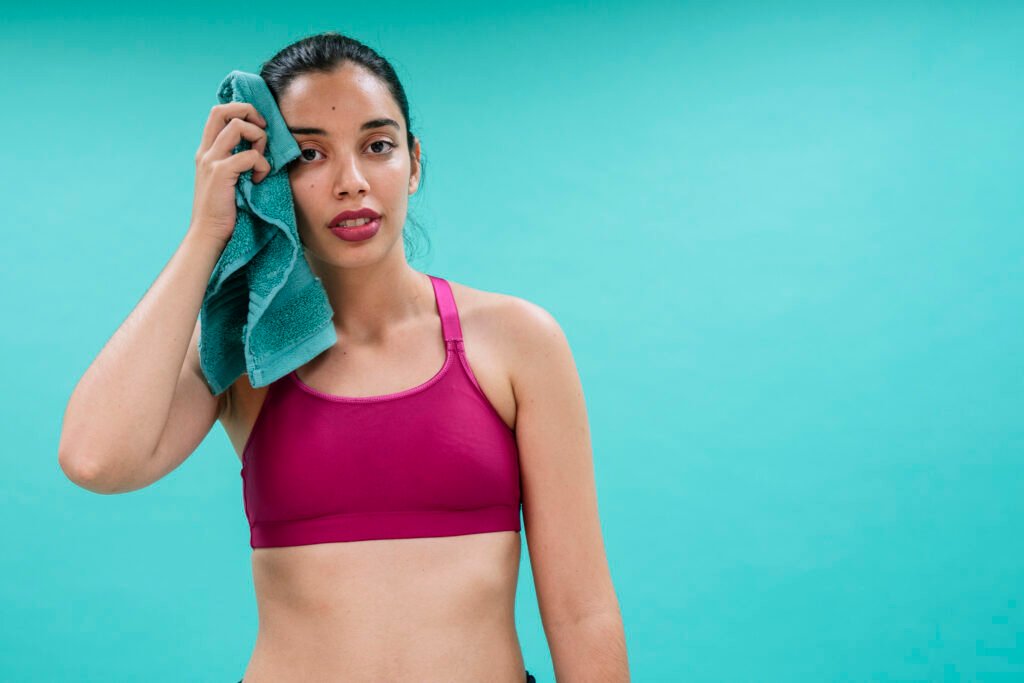  sweet sweat review Fit woman wiping sweat with towel after intense workout, wearing sports bra