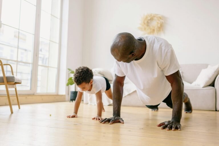A father and son bonding through exercise indoors, doing push-ups on a wooden floor.